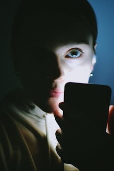 A close-up, high-contrast portrait of a person illuminated by phone light.