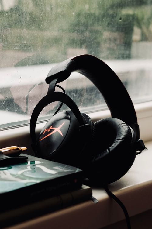 Free Black headphones resting on a window sill with a book beside them, creating a cozy ambiance. Stock Photo