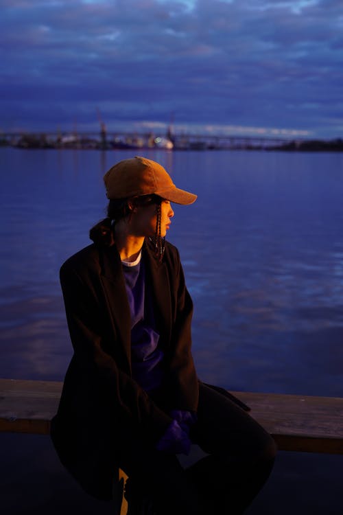 Free Man in Black Coat and Brown Hat Sitting on Brown Wooden Dock Stock Photo
