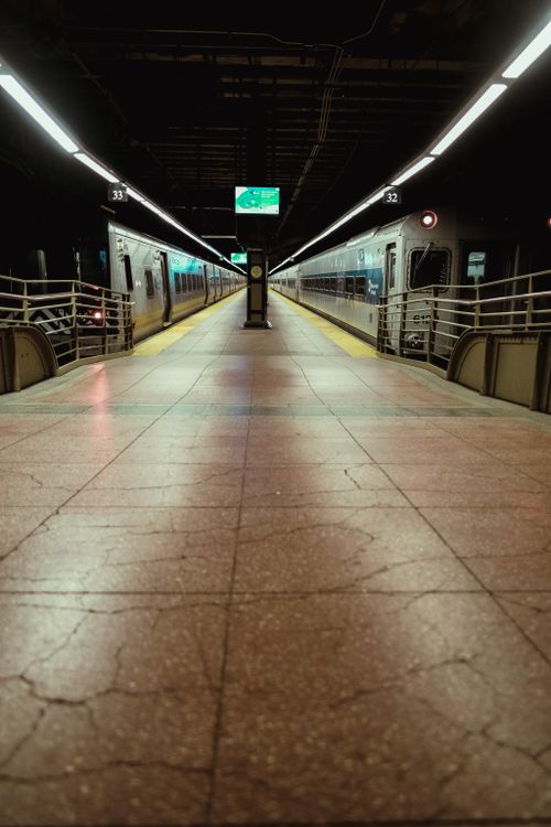 Free A deserted urban railway station platform with trains at night, featuring overhead lights and cracked flooring. Stock Photo