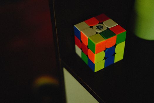 A vibrant Rubik's Cube sits on a dark shelf, showcasing its colorful puzzle design.