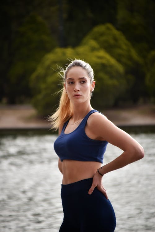 Foto de Beautiful young brunette with long hair in a sports bra and red  pants is standing on the beach. Portrait of a sports woman. do Stock