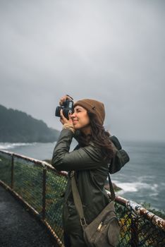 A young woman takes photos of the Oregon coastline on a cloudy day, capturing its natural beauty.