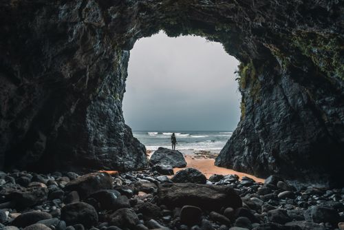 Free Person standing in a rocky cave entrance facing the ocean on an Oregon beach. Stock Photo