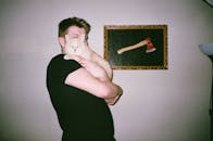 一名男子在室内抱着他的虎斑猫，背景是一幅镶框的斧头画