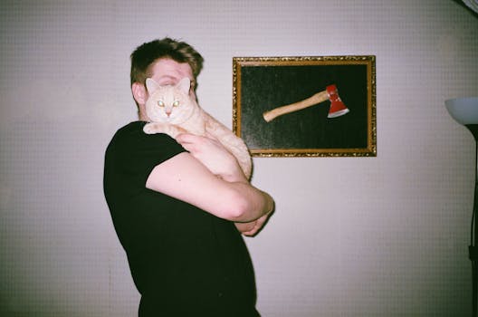 一名男子在室内抱着他的虎斑猫，背景是一幅镶框的斧头画