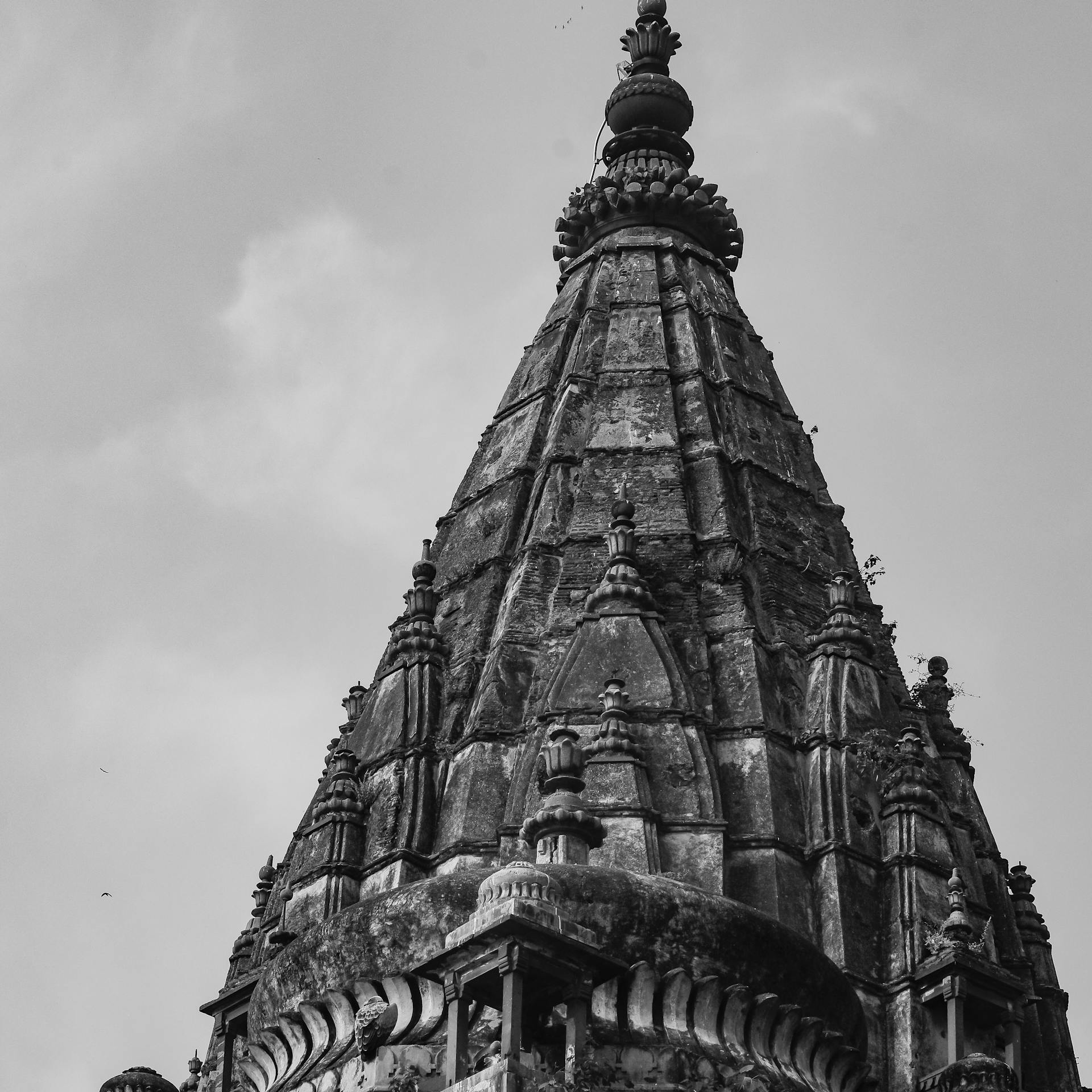 Black and white photograph capturing the intricate details of a historic temple spire against the sky.