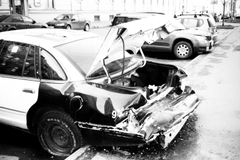 A black and white photo of a wrecked car on an urban street, highlighting vehicle damage.