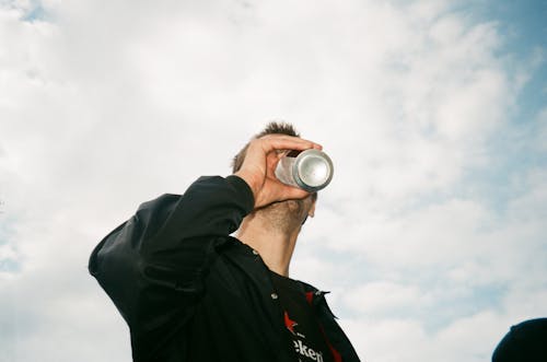 Fotografia De Baixo ângulo De Um Homem Bebendo Uma Lata Cinza Rotulada