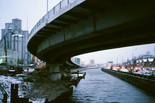 Free Concrete bridge arches over a snow-dusted canal in a bustling winter cityscape. Stock Photo
