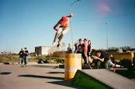 在观众簇拥下，滑板运动员于城市公园的枪管上表演了空中特技