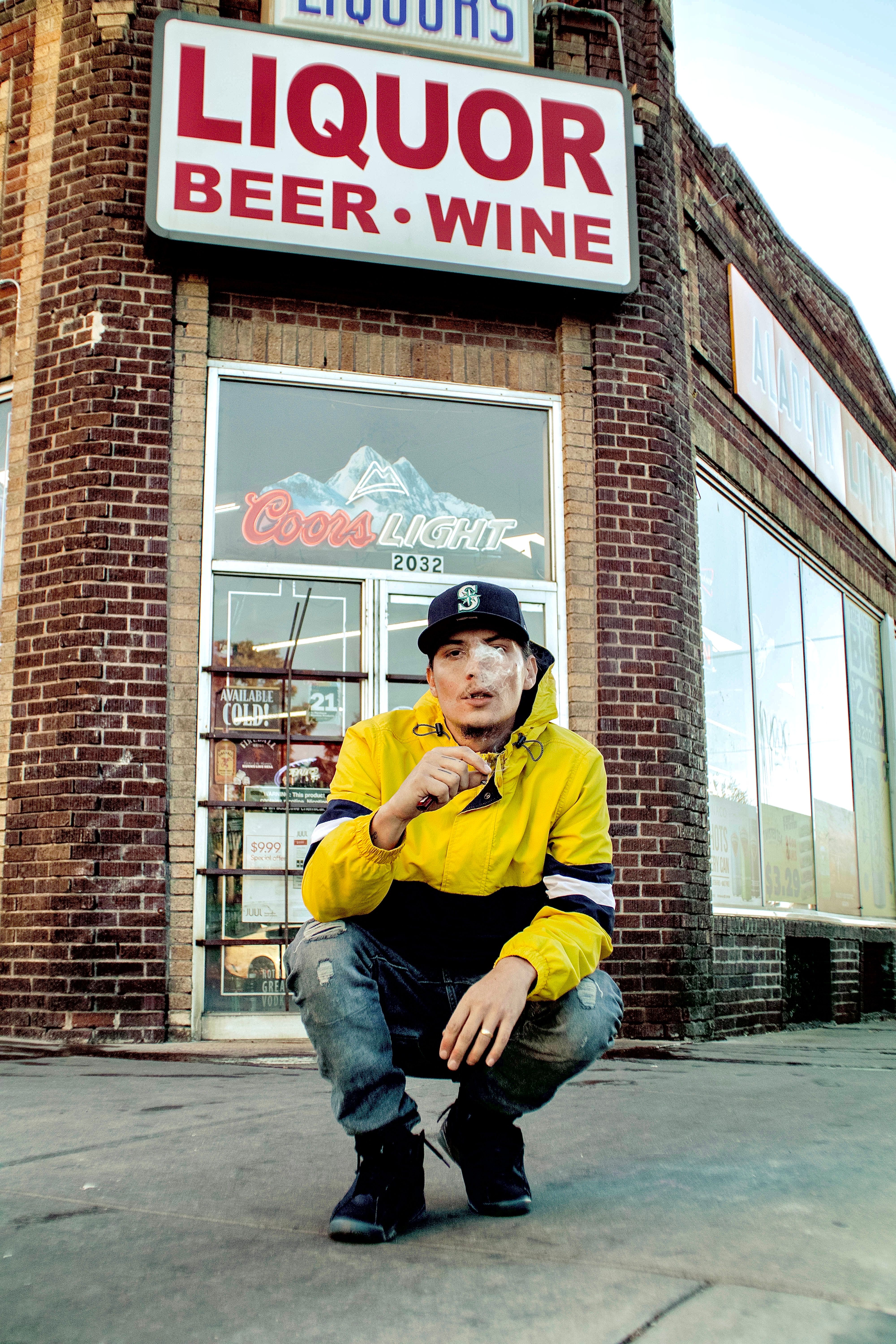Young man in a yellow jacket smokes in front of a liquor store in Denver, Colorado.