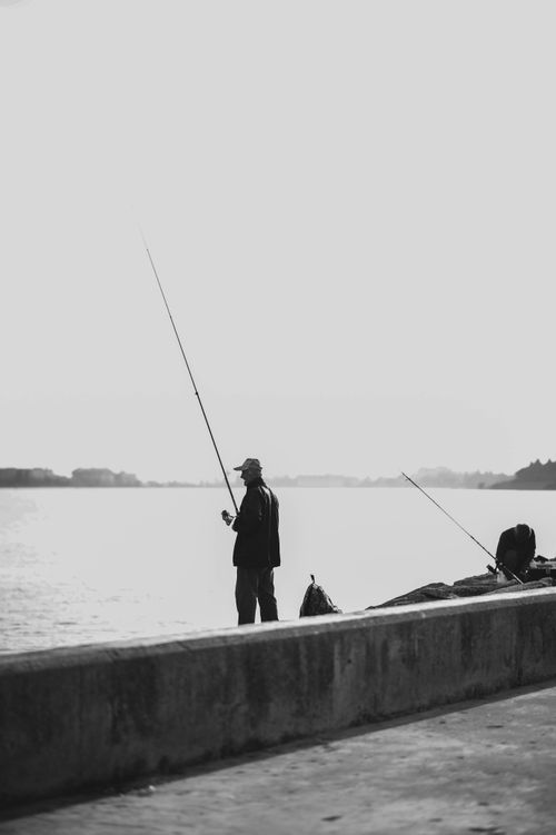 Free Black and white photo of a fisherman on a pier casting a line into the ocean. Stock Photo