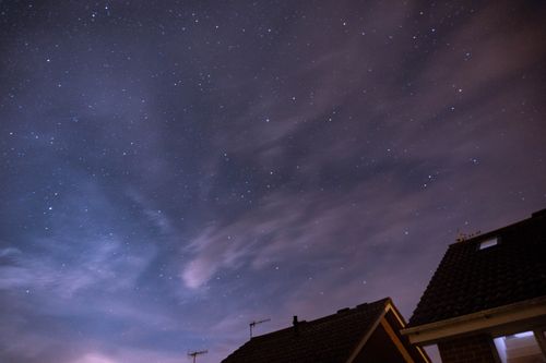 Free Long-exposure capture of a star-filled night sky with clouds and rooftops in view. Stock Photo