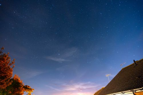 Free A star-filled night sky over suburban rooftops and trees, capturing celestial beauty. Stock Photo