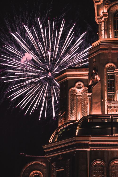 Free Dazzling fireworks light up the night sky adjacent to an ornately illuminated historic building. Stock Photo
