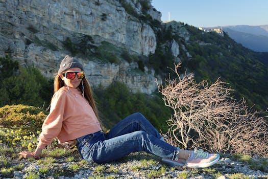 A young woman in casual attire enjoys a sunny day while seated on a mountain slope.