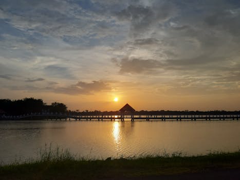 Breathtaking sunrise over a tranquil lake with a silhouetted dock in Mueang Tai, Thailand.