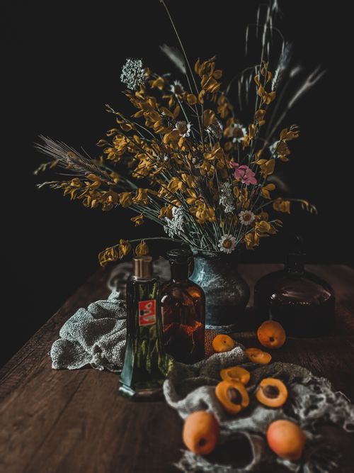 Free Artistic composition with dried flowers, apricots, and bottles on a wooden table. Stock Photo