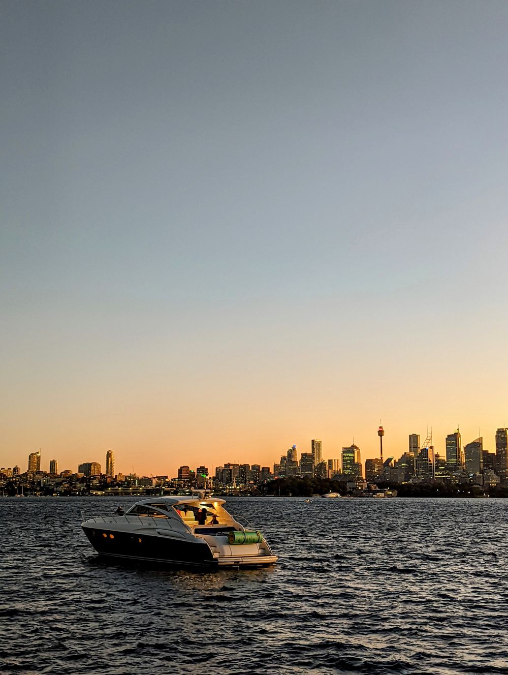 Yate de lujo cruzando la bahía de Sydney con el skyline silueteado al ocaso