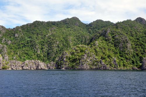 Free Serene view of rocky, forested mountains reflecting on a calm lake under a clear sky. Stock Photo
