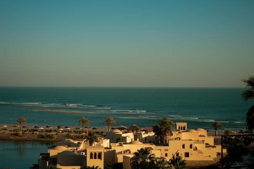 Free Beachfront resort with traditional architecture, palm trees, and a serene ocean seascape. Stock Photo
