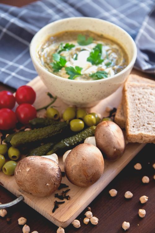 Free Bowl of homemade creamy mushroom soup garnished with parsley, surrounded by fresh vegetables on a wooden board. Stock Photo