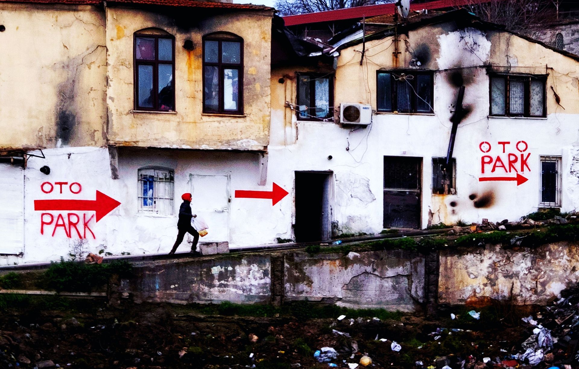 A person walks by an abandoned building with graffiti and signs in İstanbul, Turkey.