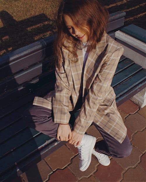 High-Angle Shot of a Girl Wearing Checkered Coat while Sitting on the Bench