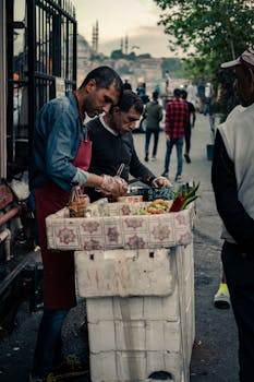 Two men selling food at a street vendor stall in an outdoor setting.