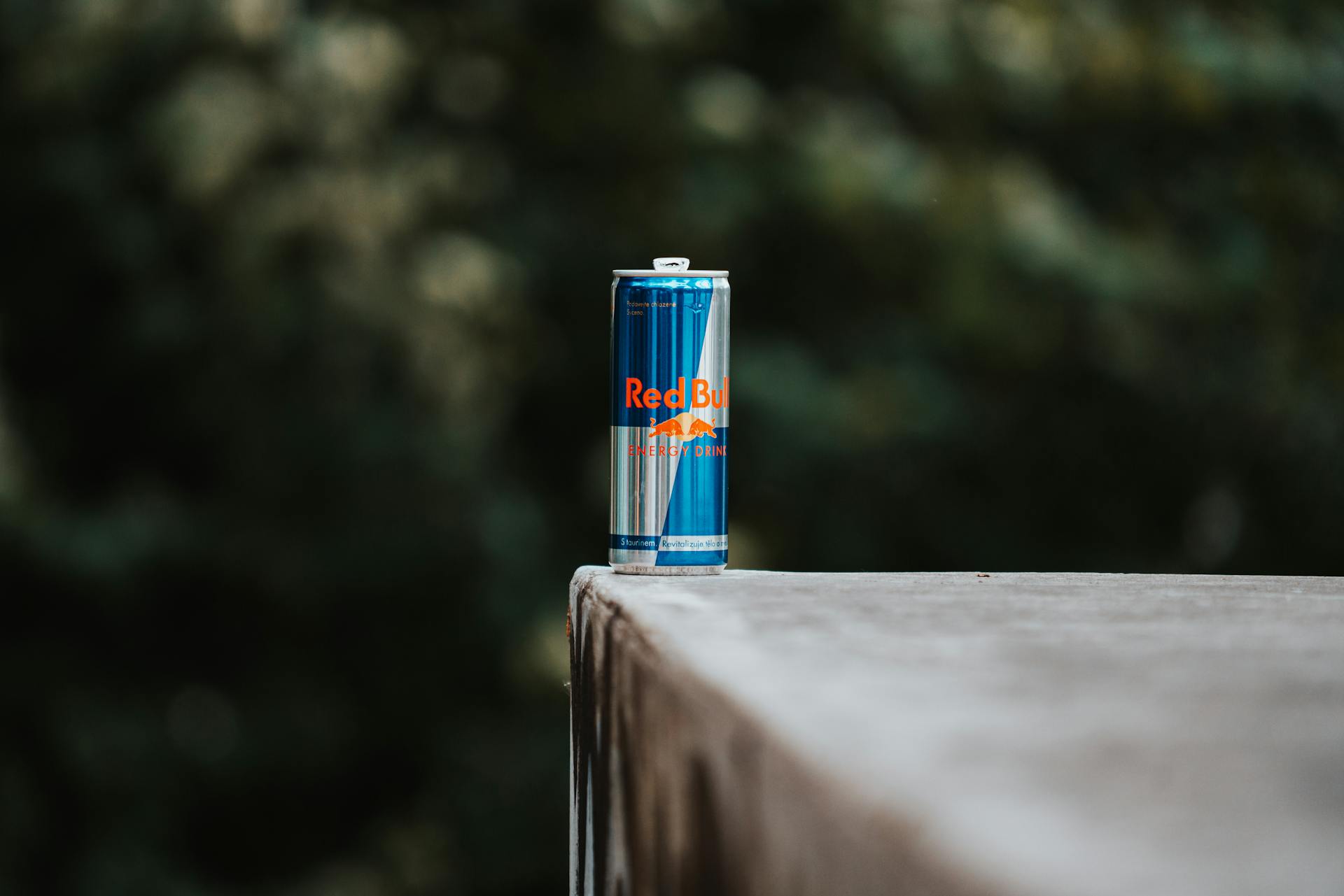 A can of energy drink on a ledge with a blurred natural background, showcasing a summer vibe.