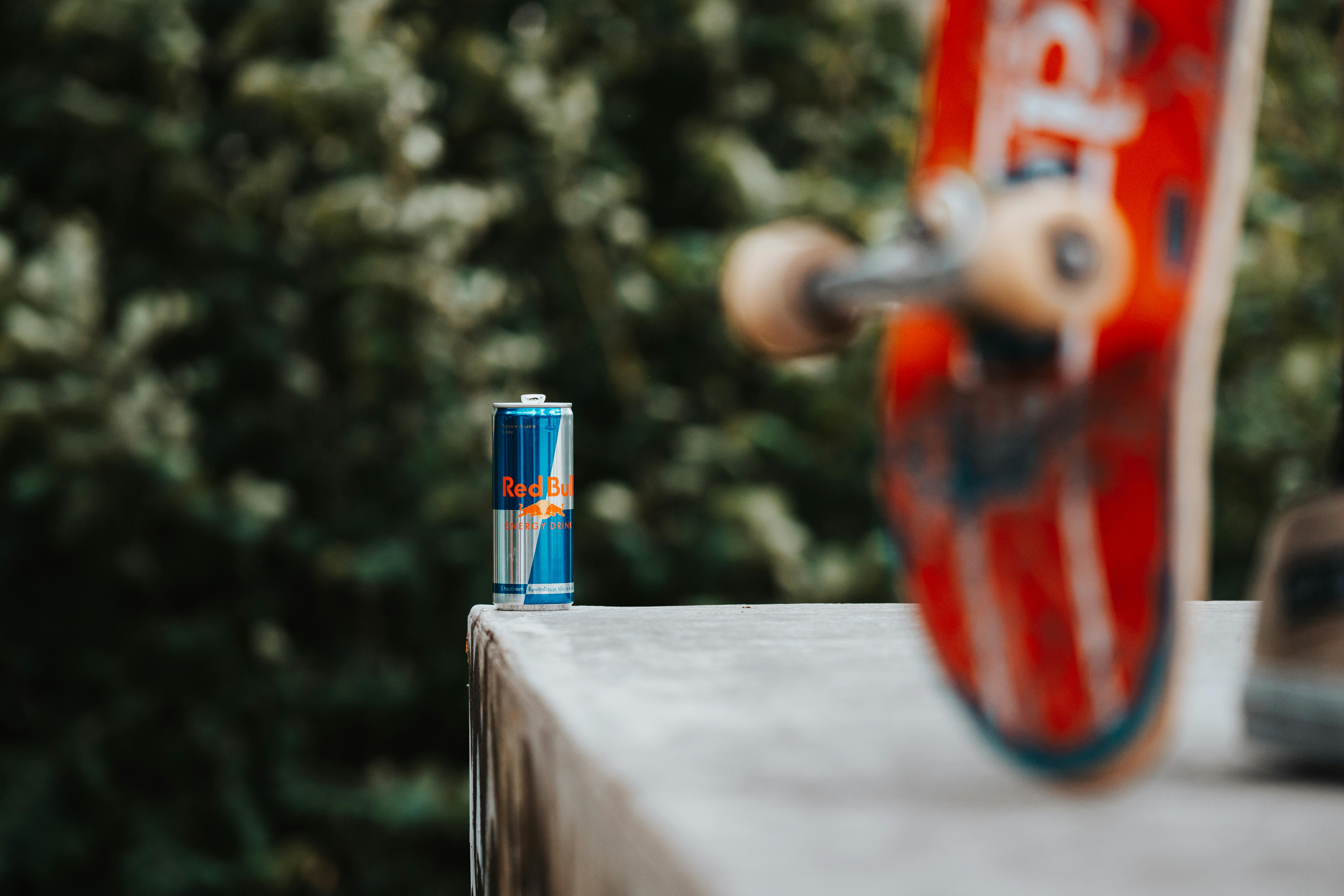 A skateboard in motion near an energy drink can, set outdoors.