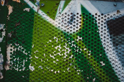 Free Green and white graffiti art creates a textured abstract pattern on a weathered metal wall. Stock Photo