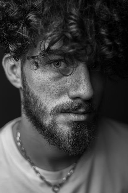 A captivating black and white portrait showcasing a man with curly hair and a beard.