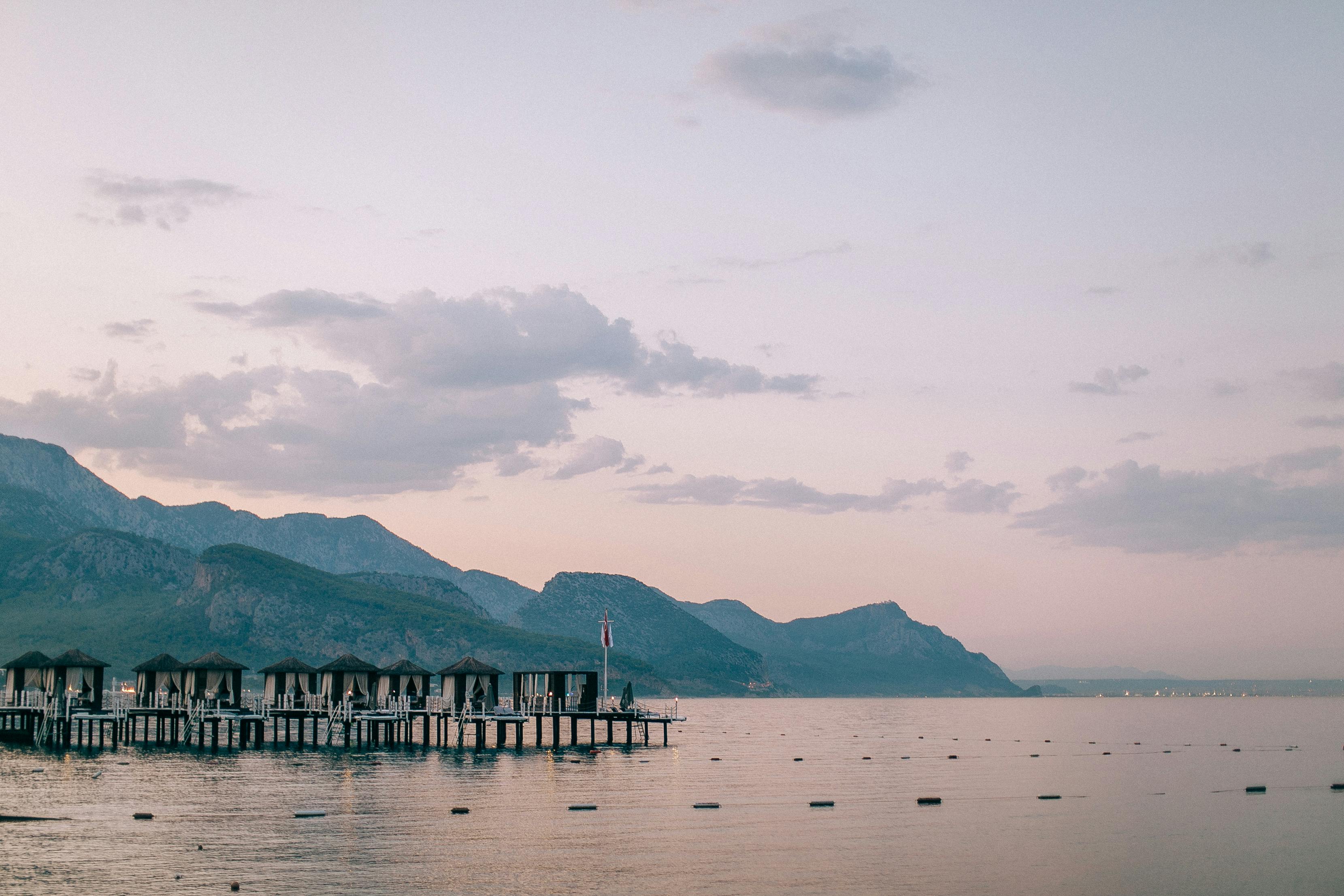 Tranquil sunset over a mountain lake with stilt houses and serene horizon view.