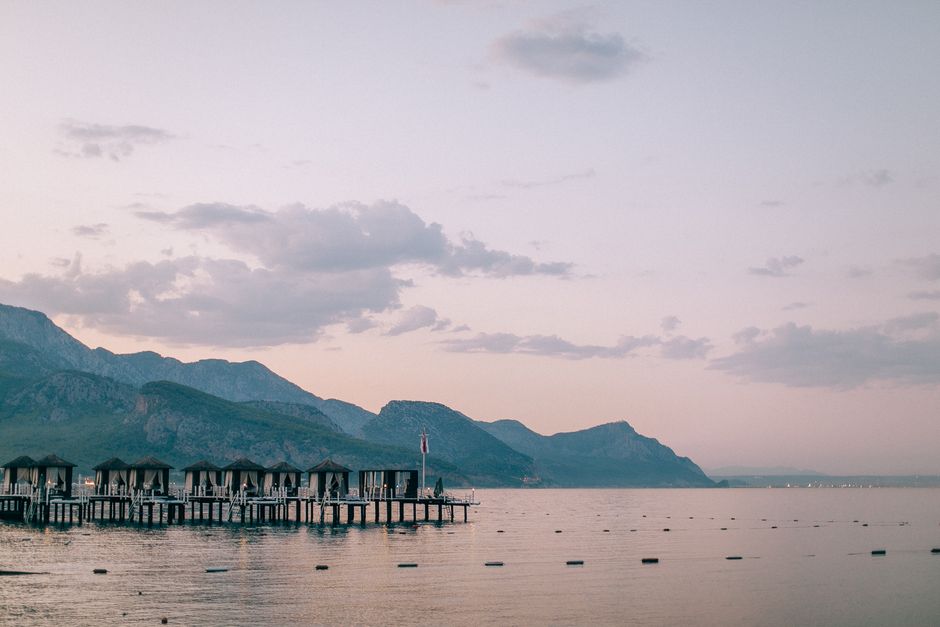 Tranquil sunset over a mountain lake with stilt houses and serene horizon view.
