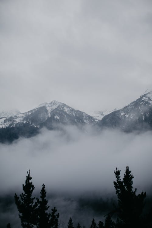 Free Snowy Mountain Tops in Fog Under a Cloudy Sky Stock Photo