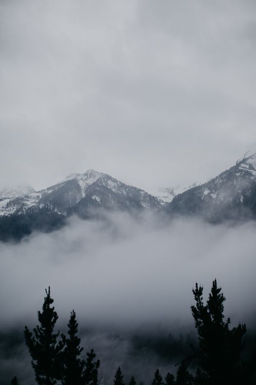 Free A dramatic, foggy mountain landscape showcasing snow-covered peaks under an overcast sky. Stock Photo