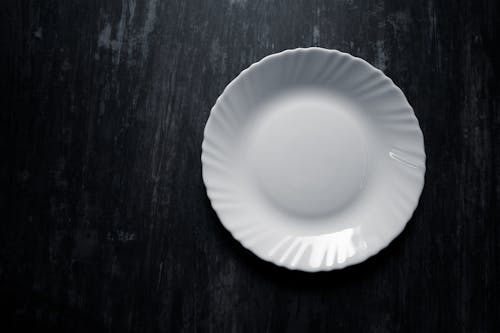Free A high-quality white ceramic plate captured from above on a textured dark background. Stock Photo