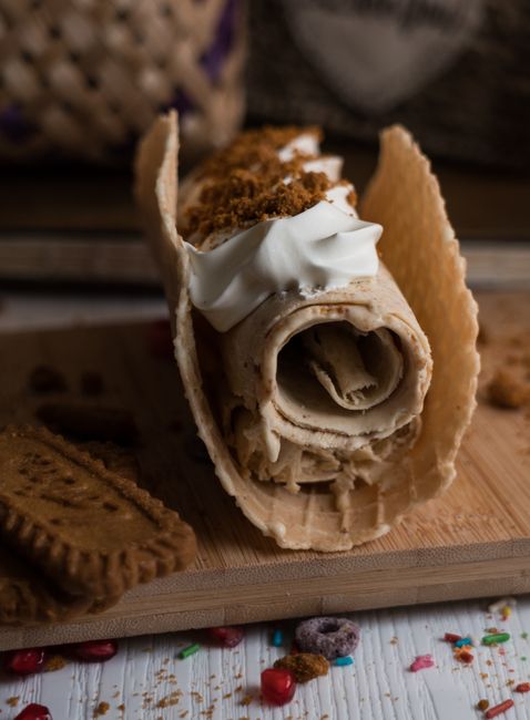 Thin, pattern-embossed krumkake cookies rolled into cone shapes, stacked beside a krumkake iron and a bowl of whipped cream.