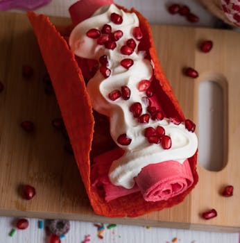 Delicious rolled ice cream topped with pomegranate seeds and whipped cream, served in a red cone.