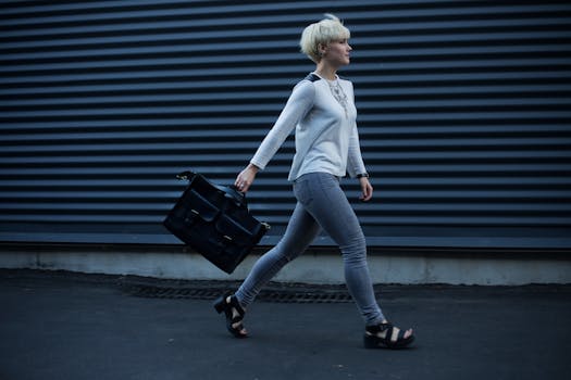 Stylish woman with blonde hair walking confidently along a city street carrying a leather bag.