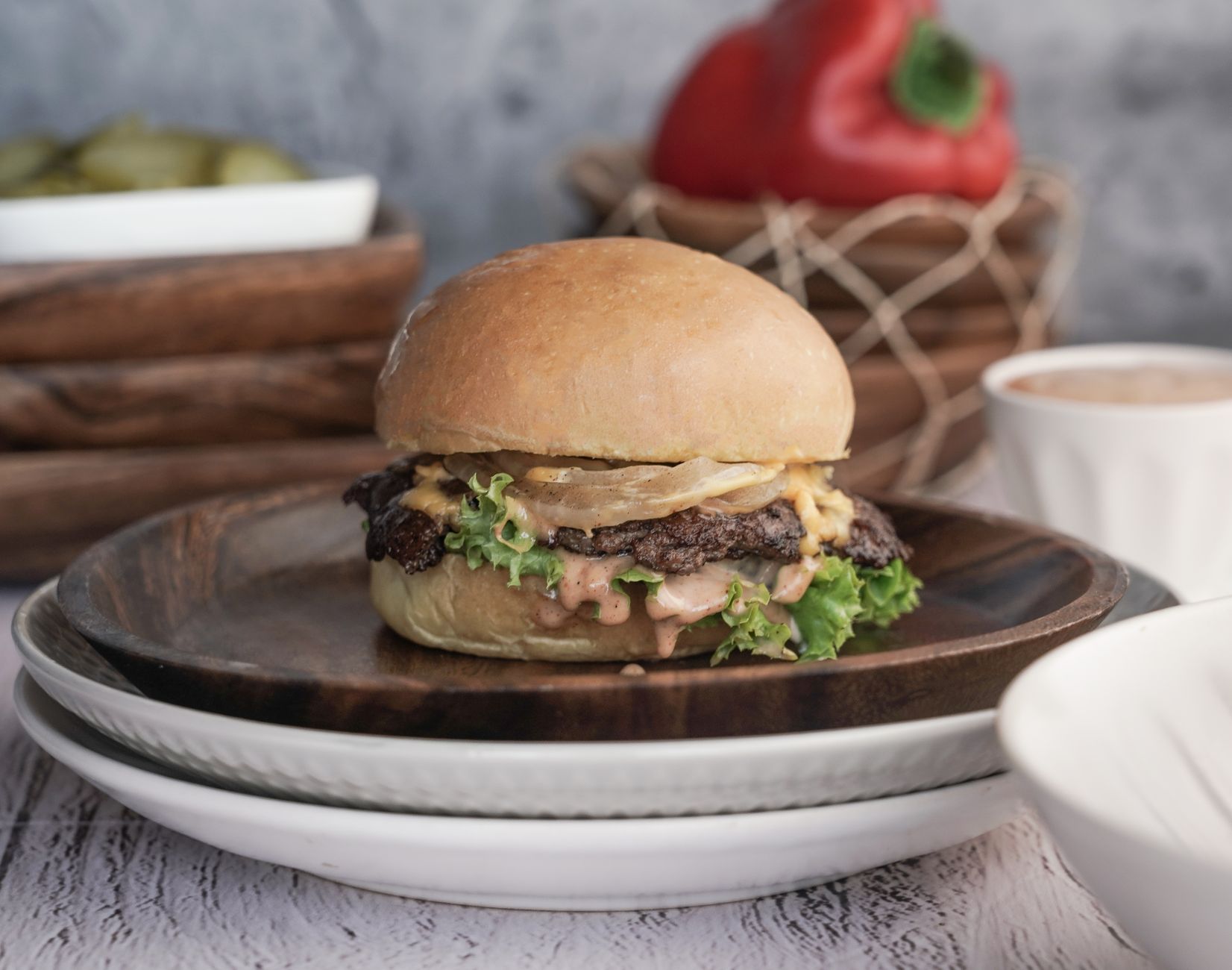 Close-up of a gourmet cheeseburger with lettuce, cheese, and sauce on a rustic wooden plate.