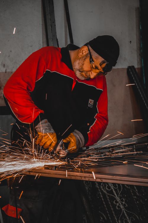 Free Senior man welding in workshop, sparks flying around, wearing safety gear. Skill and focus evident. Stock Photo
