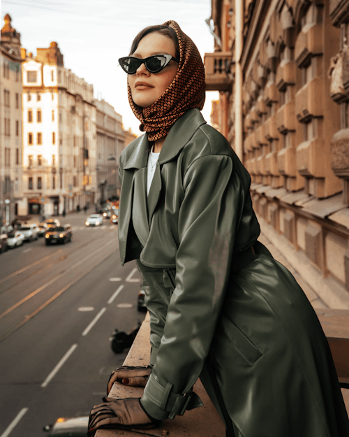 Woman in a Headscarf and Sunglasses Looking Over from a Balcony in City