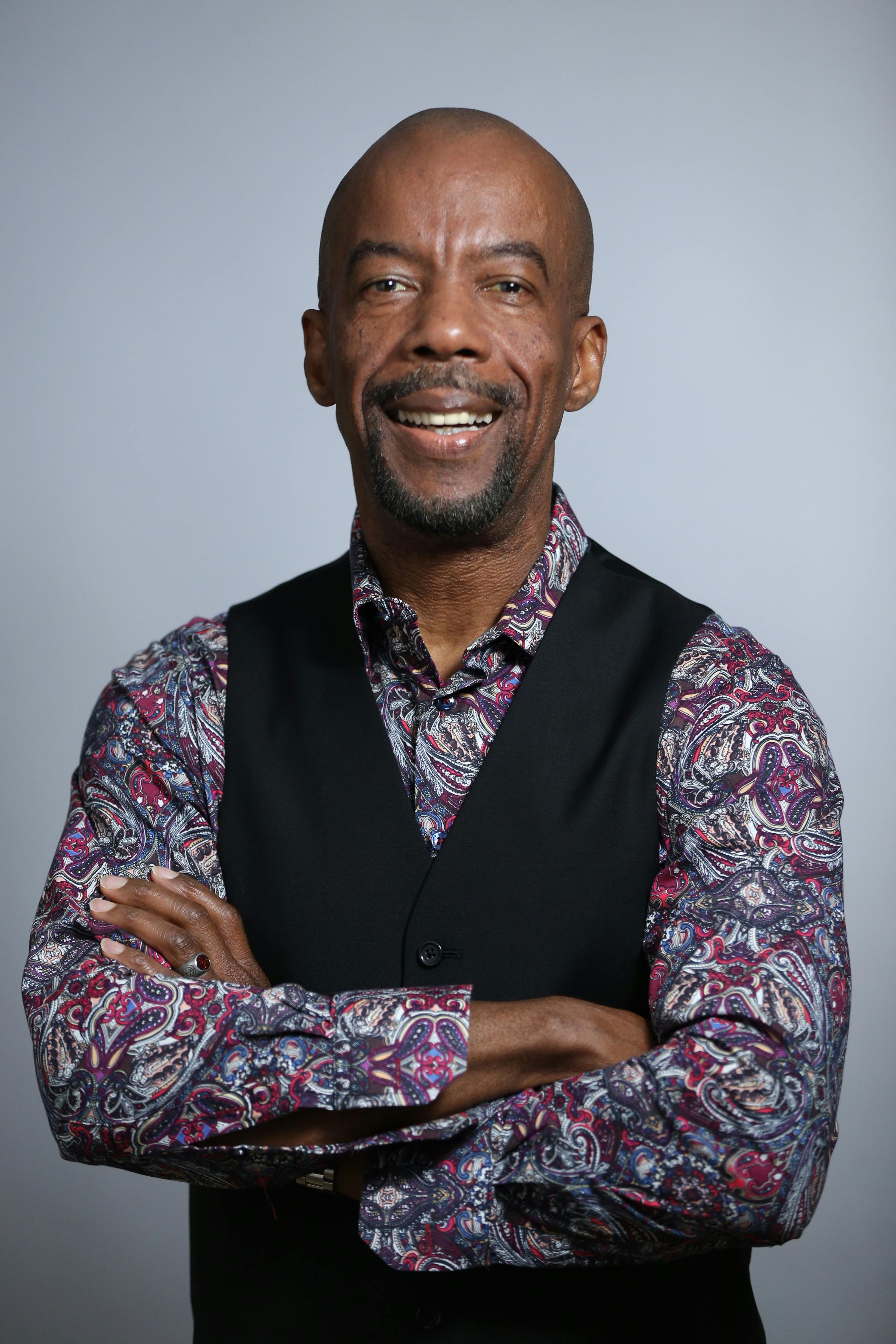 Portrait of a confident man smiling with crossed arms, wearing a patterned shirt and vest.