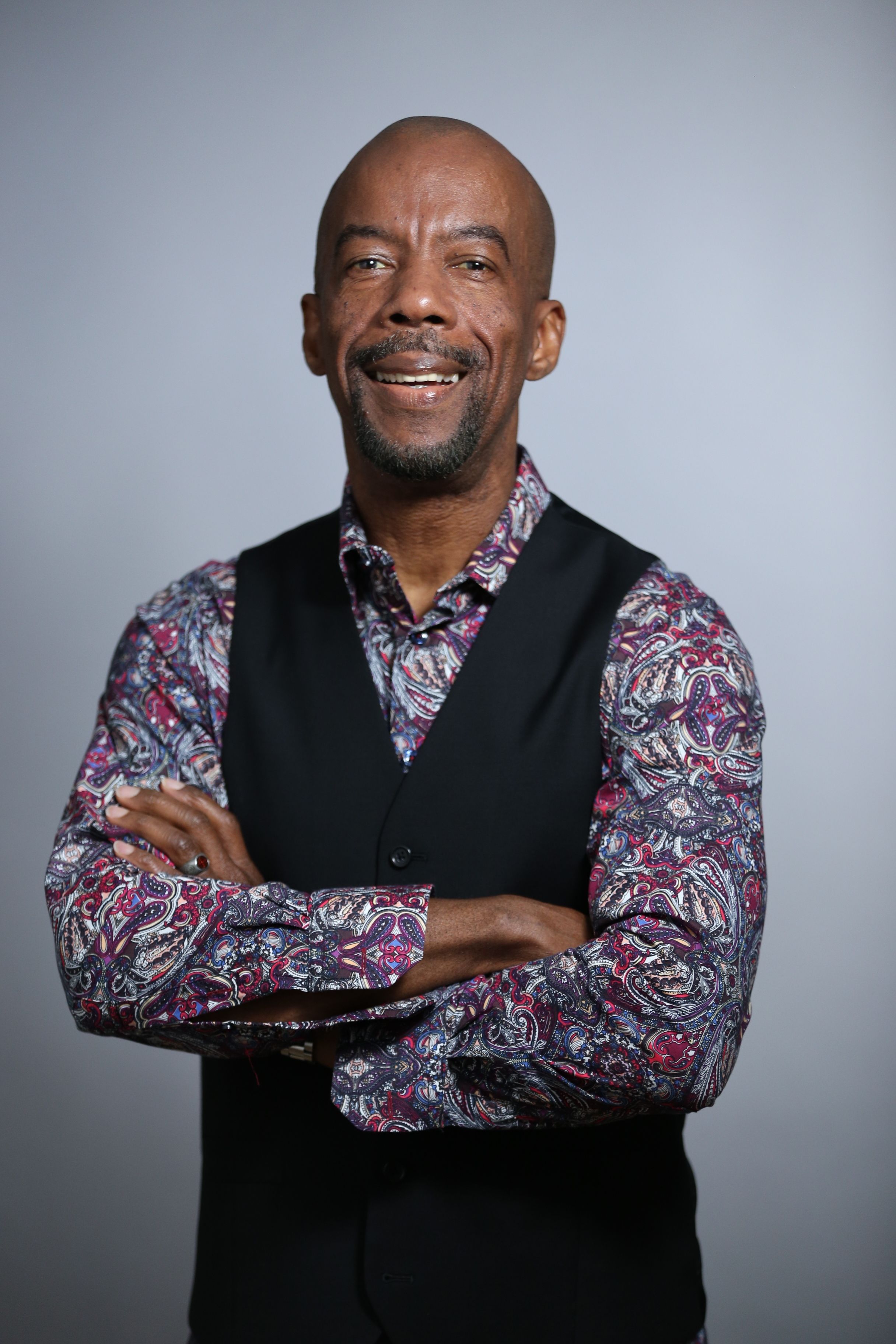 Portrait of a smiling black man in a floral shirt and vest, exuding confidence.