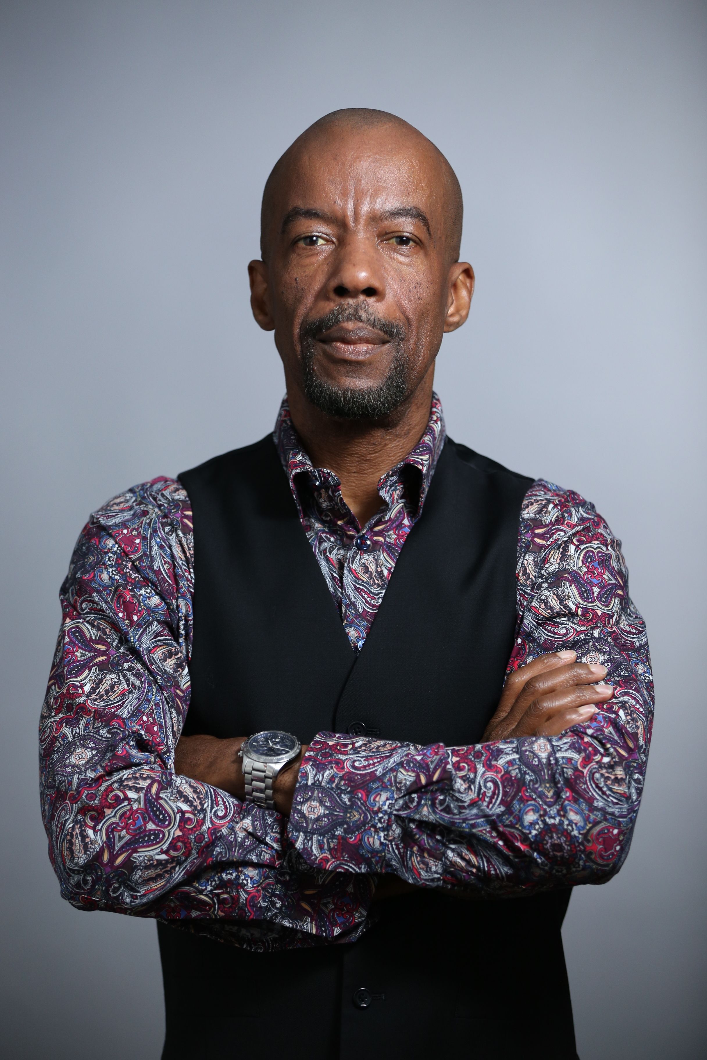 Portrait of a confident man wearing a floral long-sleeve shirt with a vest. Studio setting.