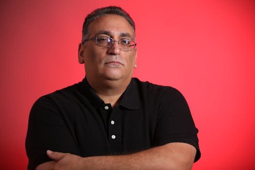 Portrait of an adult man with eyeglasses in a black polo shirt, set against a vibrant red background.