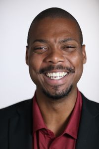 Close-up portrait of a smiling man in a black suit, exuding joy and confidence.